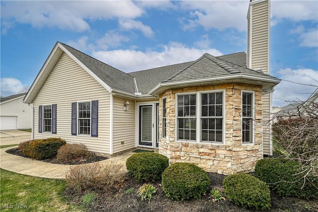 ranch-style home with stone siding, a chimney, and roof with shingles