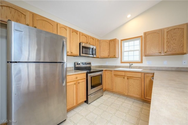 kitchen featuring lofted ceiling, stainless steel appliances, a sink, light countertops, and light floors