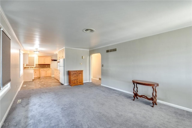 unfurnished living room with ornamental molding, arched walkways, visible vents, and light colored carpet