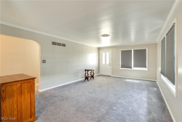 carpeted empty room with baseboards, visible vents, arched walkways, and ornamental molding