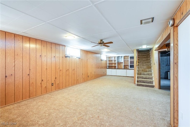 basement featuring carpet, wood walls, and stairs