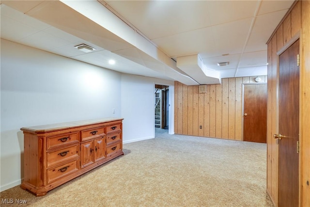 finished below grade area featuring light carpet, wood walls, baseboards, and stairway