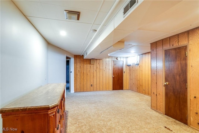 finished basement featuring carpet, visible vents, wood walls, and a drop ceiling