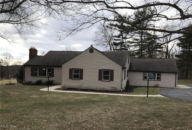 view of front of home featuring a chimney, a front lawn, and roof with shingles