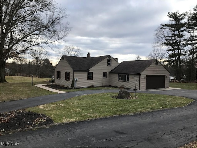 view of front of property featuring an attached garage, driveway, roof with shingles, a front lawn, and a chimney