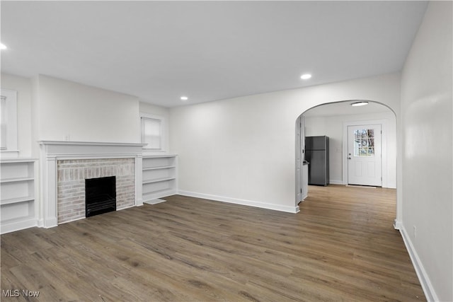 unfurnished living room with baseboards, a fireplace, arched walkways, and wood finished floors