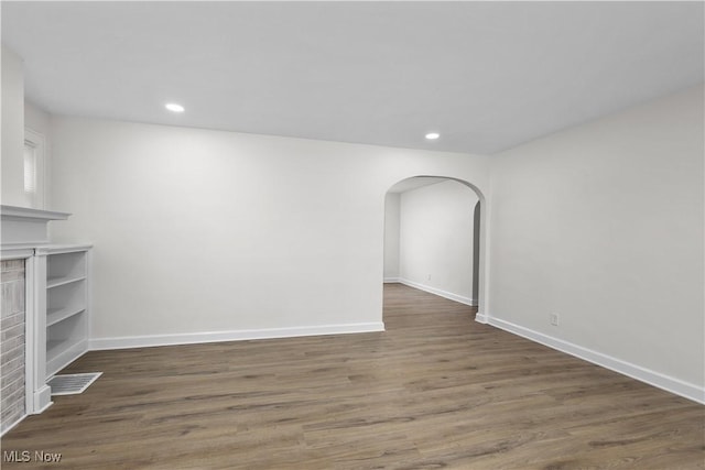 unfurnished living room featuring arched walkways, wood finished floors, and baseboards