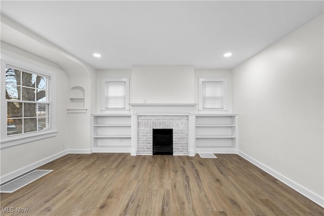 unfurnished living room featuring a fireplace, wood finished floors, visible vents, and baseboards