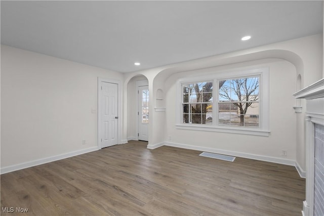 unfurnished living room featuring arched walkways, visible vents, plenty of natural light, and wood finished floors