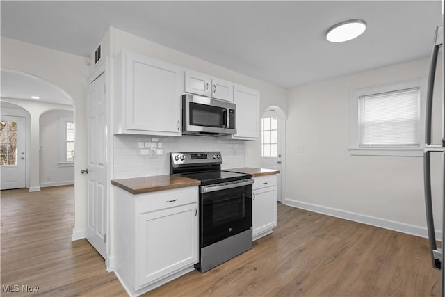 kitchen with white cabinets, tasteful backsplash, appliances with stainless steel finishes, and arched walkways