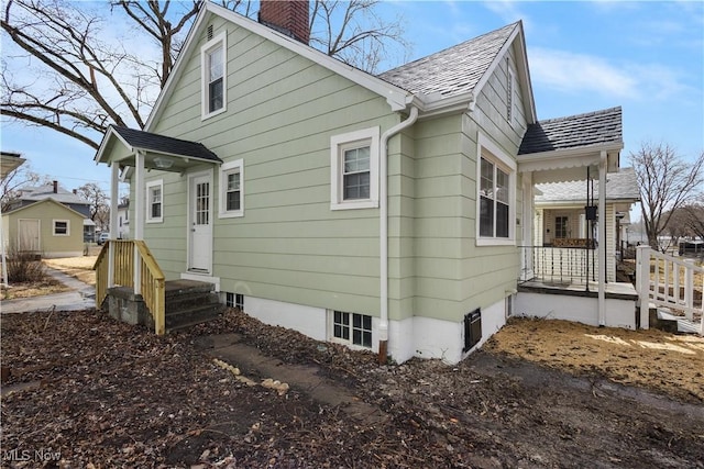 exterior space with a chimney, a porch, and roof with shingles