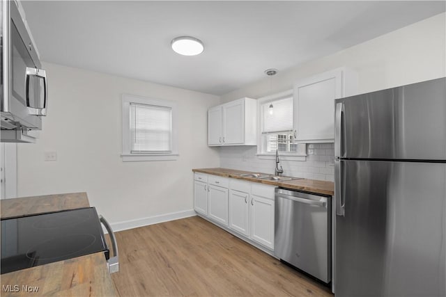 kitchen featuring butcher block countertops, a sink, white cabinetry, appliances with stainless steel finishes, and backsplash