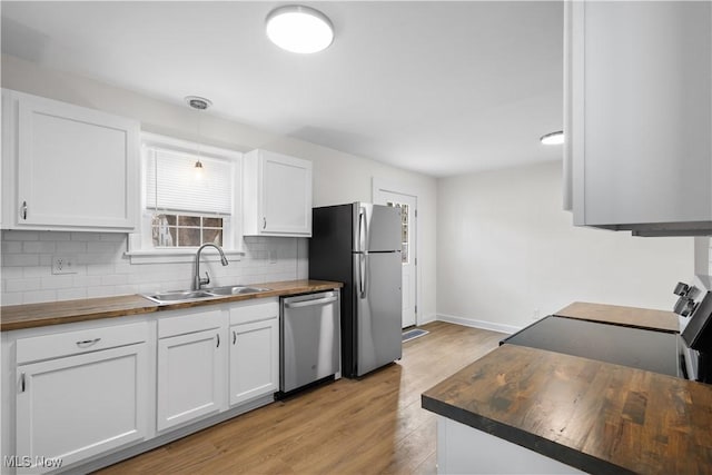 kitchen featuring butcher block counters, backsplash, appliances with stainless steel finishes, white cabinets, and a sink