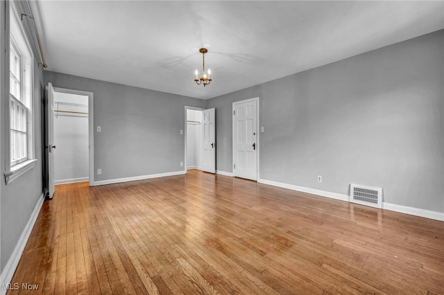 unfurnished room with light wood-style flooring, visible vents, a chandelier, and baseboards