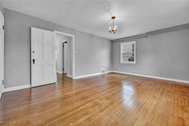 unfurnished room with baseboards, wood-type flooring, visible vents, and a notable chandelier