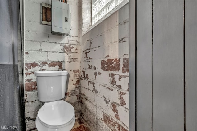 bathroom with toilet, brick wall, and electric panel