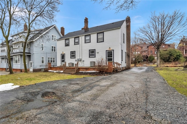 back of house with a chimney, a lawn, aphalt driveway, and cooling unit