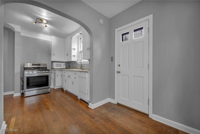 kitchen with arched walkways, white appliances, dark wood-style flooring, a sink, and white cabinets