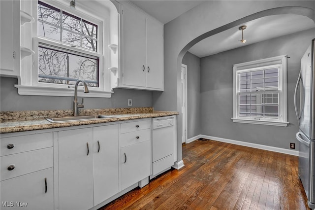 kitchen featuring arched walkways, freestanding refrigerator, a sink, dishwasher, and baseboards