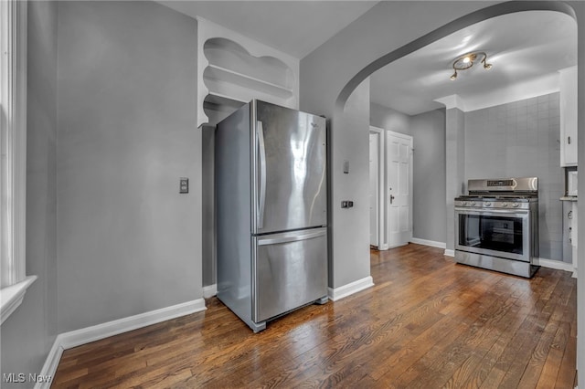 kitchen featuring arched walkways, appliances with stainless steel finishes, dark wood finished floors, and baseboards