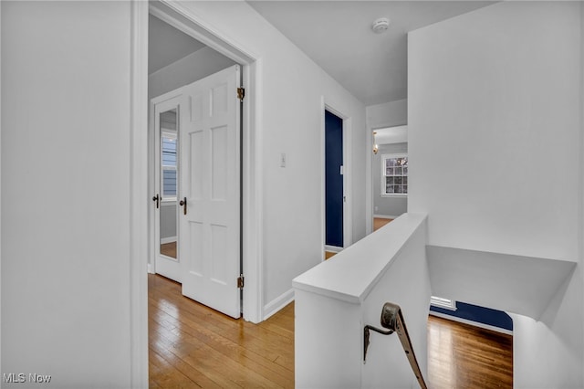 corridor featuring light wood-style flooring, baseboards, and an upstairs landing