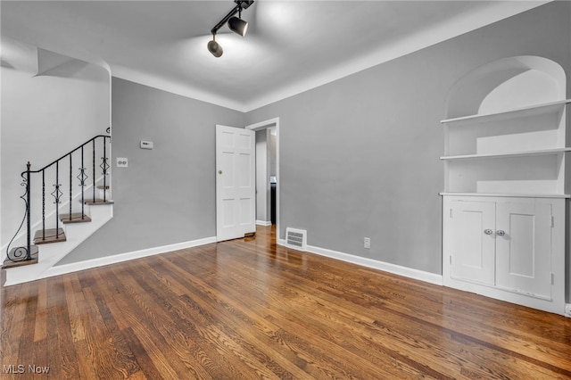 unfurnished living room with rail lighting, visible vents, wood finished floors, baseboards, and stairs