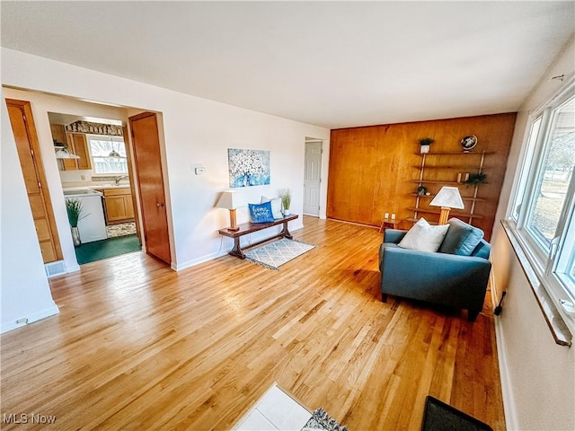 living area featuring light wood-type flooring, wooden walls, and baseboards