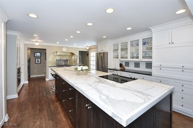 kitchen featuring high quality fridge, black electric cooktop, a spacious island, a sink, and white cabinets