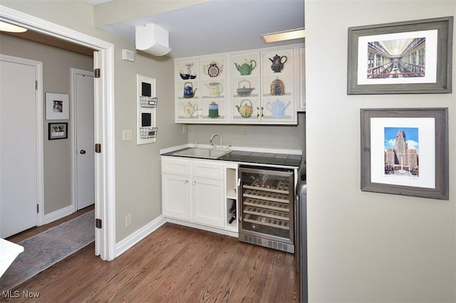 bar featuring wine cooler, indoor wet bar, dark wood finished floors, a sink, and baseboards