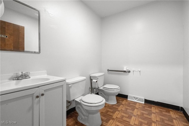 bathroom with toilet, vanity, visible vents, and baseboards