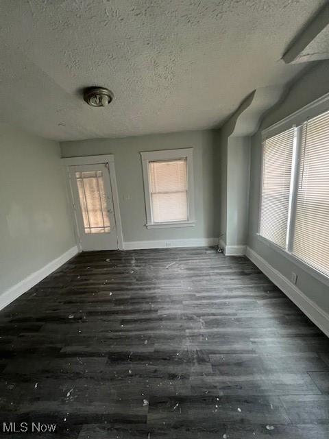 empty room featuring dark wood-style flooring, a textured ceiling, and baseboards