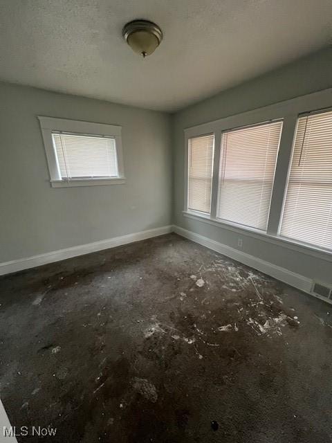 unfurnished room with visible vents, a textured ceiling, and baseboards