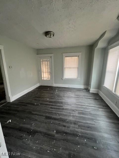 unfurnished room with a textured ceiling, baseboards, and wood finished floors