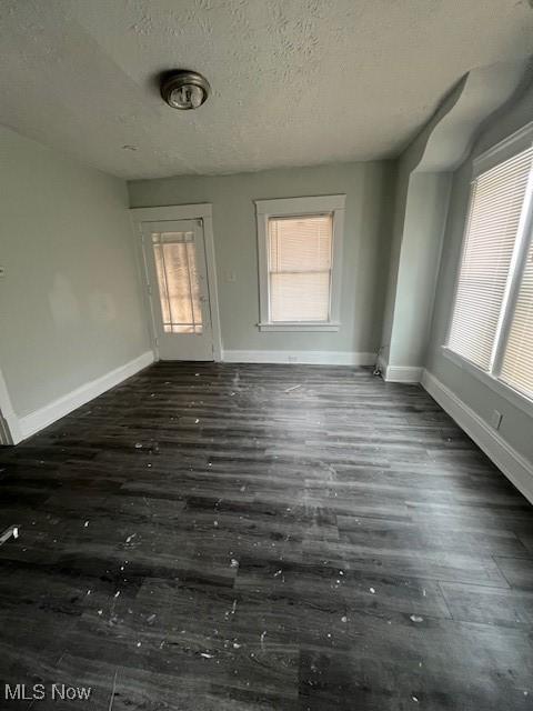 empty room with dark wood finished floors, a textured ceiling, and baseboards