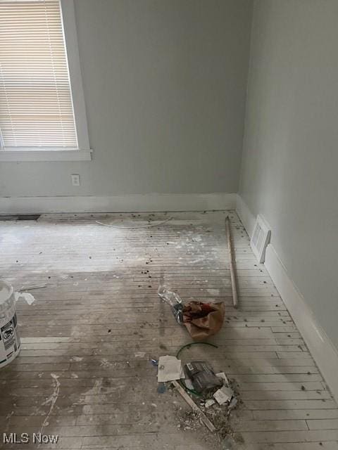 empty room featuring wood-type flooring, visible vents, and baseboards