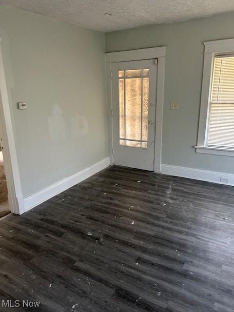 spare room with a textured ceiling, wood finished floors, baseboards, and a healthy amount of sunlight