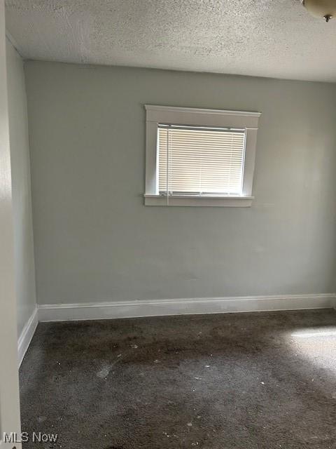 carpeted spare room featuring baseboards and a textured ceiling