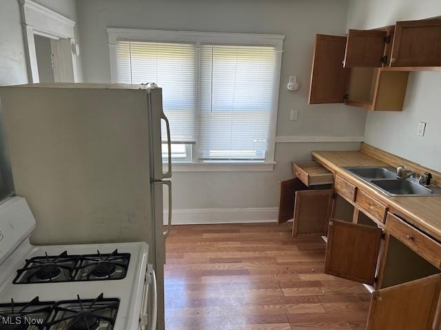 kitchen with light wood-style floors, white range with gas cooktop, light countertops, a sink, and baseboards