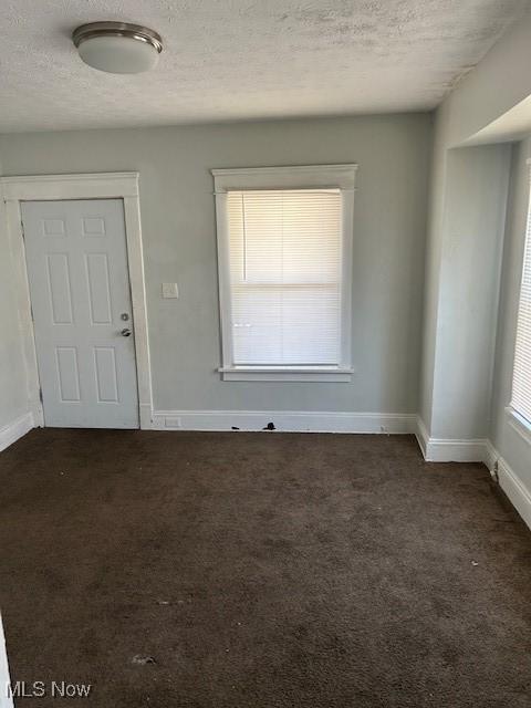 unfurnished room featuring dark carpet, a textured ceiling, and baseboards