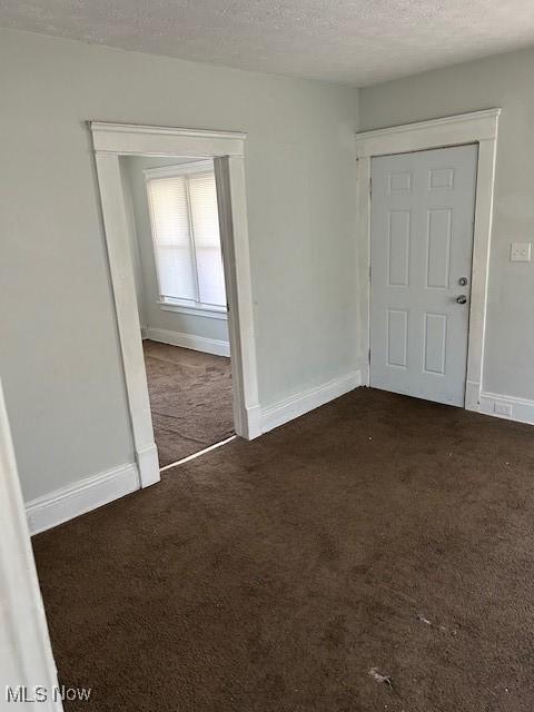 spare room with a textured ceiling, dark colored carpet, and baseboards