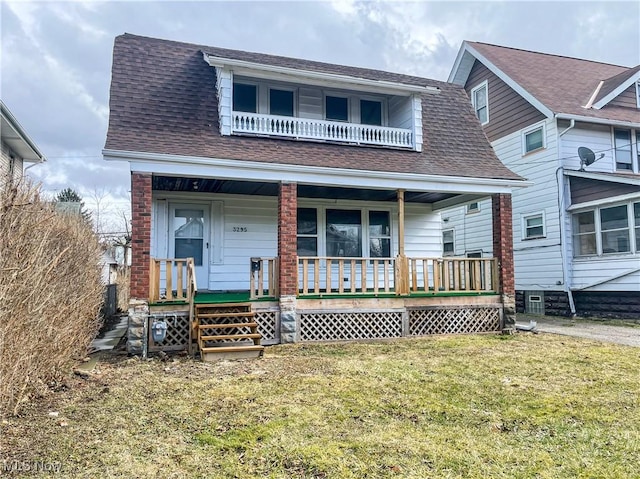 view of front facade with a shingled roof, a front yard, covered porch, and a balcony