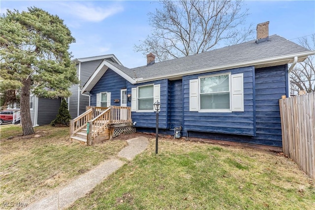 ranch-style house featuring roof with shingles, fence, a chimney, and a front lawn