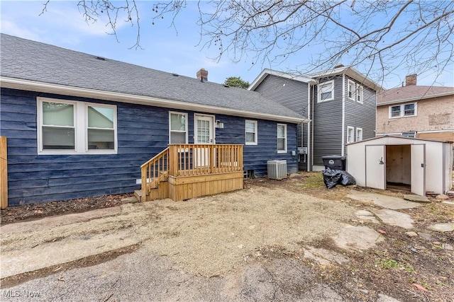 exterior space featuring a storage unit, central AC unit, an outdoor structure, and a shingled roof