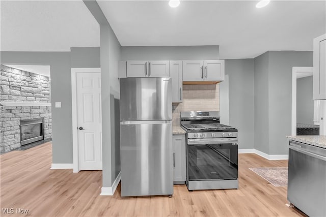 kitchen with gray cabinetry, a fireplace, light wood-style floors, appliances with stainless steel finishes, and tasteful backsplash