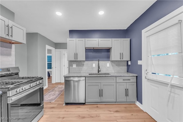 kitchen featuring baseboards, light stone counters, stainless steel appliances, light wood-type flooring, and a sink