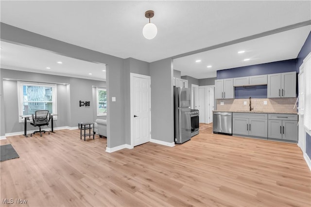 kitchen featuring stainless steel appliances, a sink, baseboards, light wood-type flooring, and tasteful backsplash