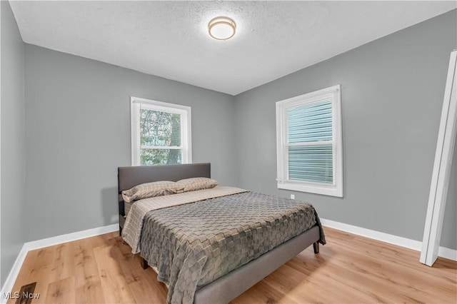 bedroom featuring light wood-type flooring, a textured ceiling, and baseboards