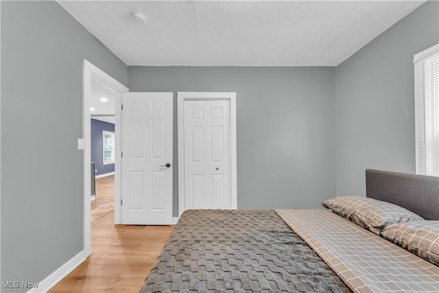 bedroom with light wood-style floors, a textured ceiling, and baseboards