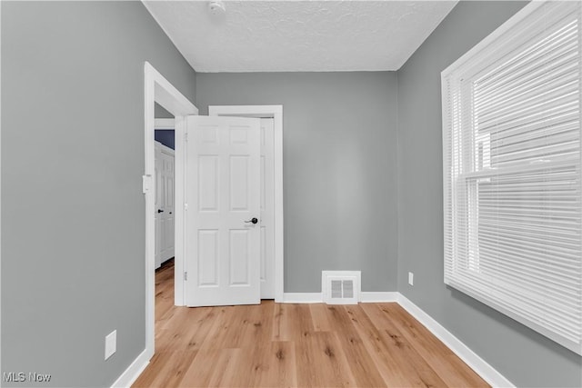 spare room with light wood-style floors, visible vents, a textured ceiling, and baseboards