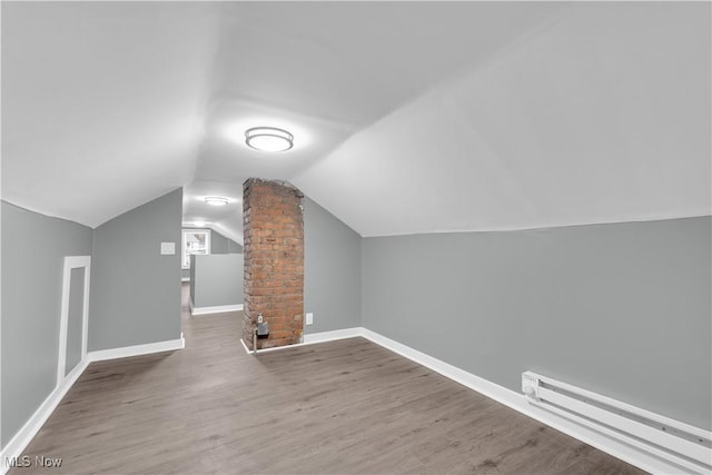 additional living space with baseboards, a baseboard heating unit, vaulted ceiling, and wood finished floors